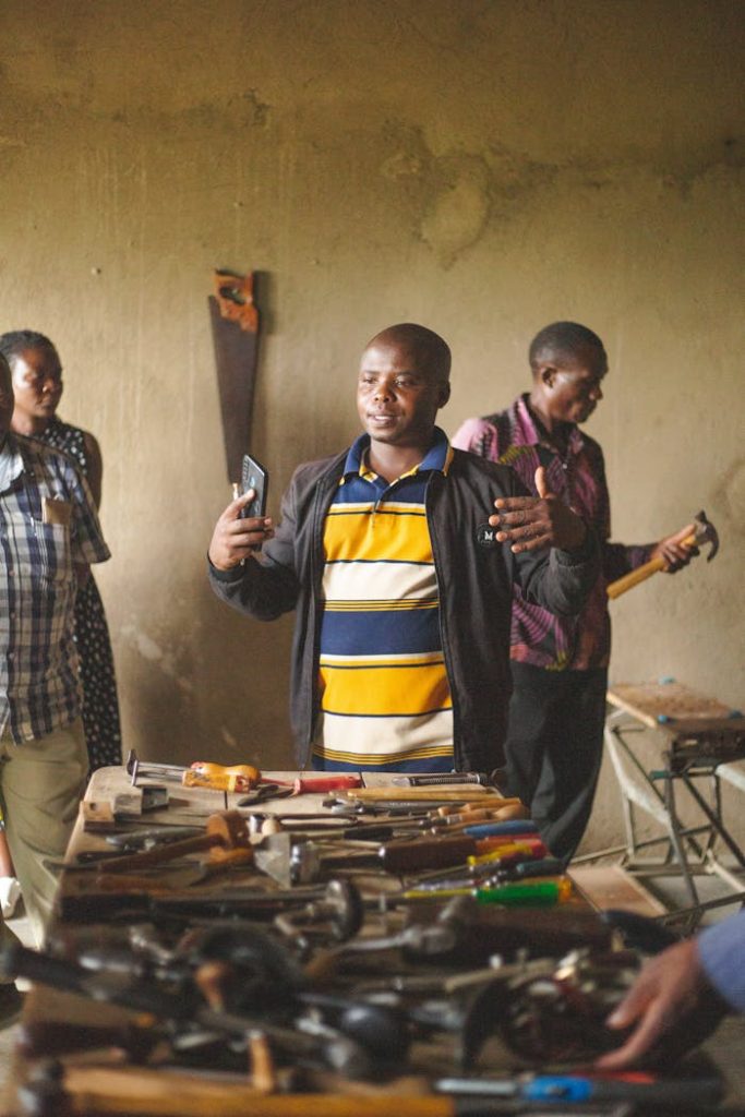 Adults engaged in a community workshop session in Kasese, Uganda surrounded by hand tools. Indoor setting.